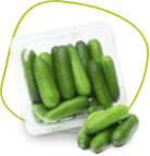 A transparent plastic container filled with fresh, small green cucumbers, with a few cucumbers placed outside the container on a flat surface. The background is a vibrant, stylized green and yellow pattern. GREENHOUSE Goodness